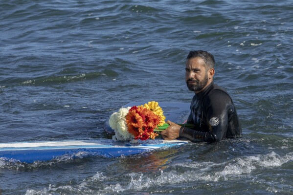 A man holds flowers during a tribute to 3 missing surfers in Ensenada, Mexico, Sunday, May 5, 2024. Mexican authorities said Friday that three bodies were recovered in an area of Baja California near where two Australians and an American went missing last weekend during an apparent camping and surfing trip. (AP Photo/Karen Castaneda)