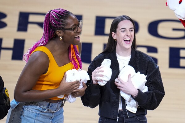 Indiana Fever players Aliyah Boston, left, and Caitlin Clark throw tee-shirts to fans during a time out during the first half between the Indiana Pacers and the Milwaukee Bucks in Game 2 in an NBA basketball first-round playoff series, Friday, April 26, 2024, in Indianapolis. (AP Photo/Michael Conroy)
