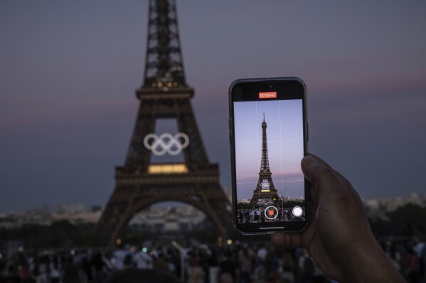 A person takes video of Olympic rings on the Eiffel Tower Friday, June 7, 2024, in Paris. The Paris Olympics organizers mounted the rings on the Eiffel Tower on Friday as the French capital marks 50 days until the start of the Summer Games. The 95-foot-long and 43-foot-high structure of five rings, made entirely of recycled French steel, will be displayed on the south side of the 135-year-old historic landmark in central Paris, overlooking the Seine River. (AP Photo/Aurelien Morissard)