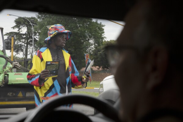 A man distributing pamphlets at a busy traffic intersection seen from a private security vehicle east of Johannesburg, South Africa, Tuesday, Nov. 28, 2023.  (AP Photo/Denis Farrell)