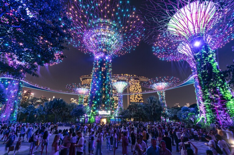 Visitors walk beneath the "Supertrees" during a light and sound show at Gardens By The Bay in Singapore, Monday, July 17, 2023. The giant structures are meant to mimic real life trees by providing shade from the sun while also capturing the sun's energy using solar panels at the top. They range in size from the tallest, at around 50 meters (164 feet), down to 25 meters (82 feet) tall. The structures are part of Singapore's vision of being "a city in a garden." (AP Photo/David Goldman)