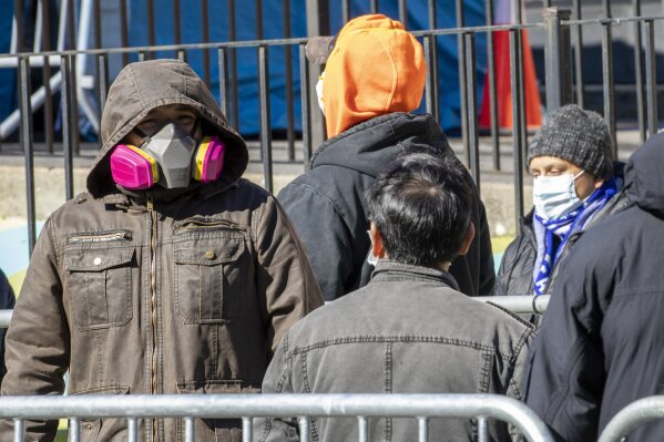 People wear face masks as they line up outside Elmhurst Hospital Center to be tested for the coronavirus, Tuesday, March 24, 2020, in the Queens borough of New York. New York Gov. Andrew Cuomo said the number of positive coronavirus cases in the state surged to more than 20,000, with more than half the cases in New York City. (AP Photo/Mary Altaffer)
