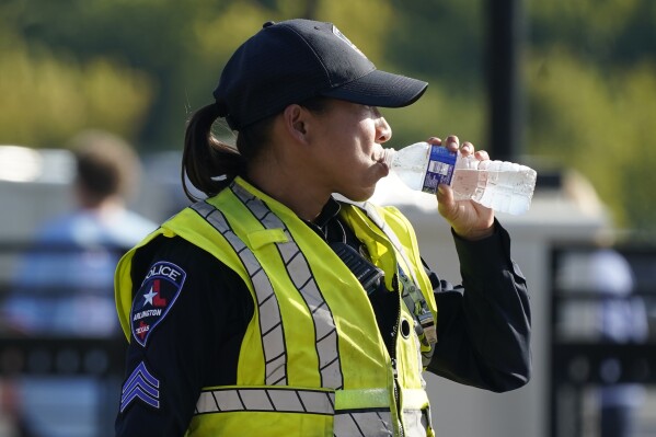 A police officer directing traffic takes a break to drink water after a sporting event in Arlington, Texas, Saturday, Aug. 19, 2023. The summer of 2023 may be drawing to a close — but the extreme heat is not: More record-shattering temperatures — this time across Texas — are expected Saturday and Sunday as the U.S. continues to bake. (AP Photo/LM Otero)