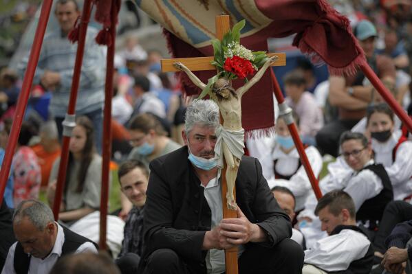 A man holds a crucifix as Catholic pilgrims fill the hillsides after tens of thousands joined their faith's biggest religious event in Sumuleu Ciuc, Romania, Saturday, May 22, 2021. More than 35,000 Catholic pilgrims congregated at an open-air shrine in Sumuleu Ciuc in Transylvania on Saturday for an age-old procession that last year was canceled due to the coronavirus pandemic. (AP Photo/Vadim Ghirda)
