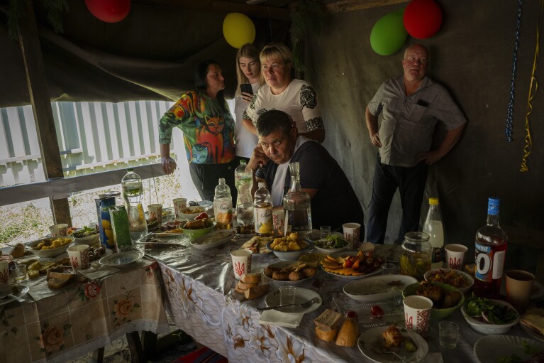 Family members sit at the wedding lunch of Ukrainian soldier Ivan Soroka and his wife Vladislava Ryabets during the second day of their wedding in the outskirt of Kyiv, Ukraine on Sunday, Sept. 10, 2023. (AP Photo/Bela Szandelszky)