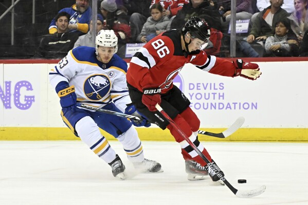 New Jersey Devils center Jack Hughes (86) controls the puck as he is checked by Buffalo Sabres left wing Jeff Skinner (53) during the first period of an NHL hockey game Saturday, Nov. 25, 2023, in Newark, N.J. (AP Photo/Bill Kostroun)