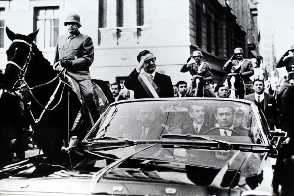 FILE - Chilean President Salvador Allende salutes from an open vehicle as General Augusto Pinochet rides on horseback at left in Santiago, Chile, May 21, 1972. (AP Photo/File)