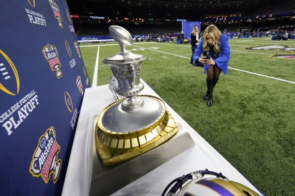 Katie Feeney, a social media reporter, films the Sugar Bowl trophy during media day for the the upcoming Sugar Bowl NCAA CFP college football semi-final game between Texas and Washington in New Orleans, Saturday, Dec. 30, 2023. (AP Photo/Gerald Herbert)