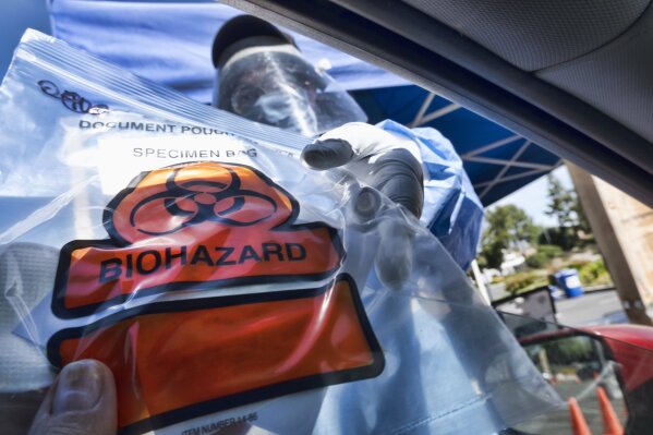 FILE -In this May 6, 2020 photo a medical worker hands a self administered coronavirus test to a patient at a drive through testing site in a parking lot in the Woodland Hills section of Los Angeles. California's death count from the coronavirus surpassed 15,000 on Sunday, Sept. 20, even as the state saw widespread improvement in infection levels. (AP Photo/Richard Vogel, File)