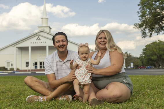 Sam Earle, left, and his wife, Tori, pose with their daughter, Novalie, outside the Heritage Baptist Church Tuesday, May 7, 2024, in Lakeland, Fla. Novalie was born through an embryo adoption. “We’re believers,” says Tori, 30, who belongs to the Baptist church where her dad once was pastor. “So we just prayed about it, and we asked the Lord to just kind of guide us.” (AP Photo/Mike Carlson)
