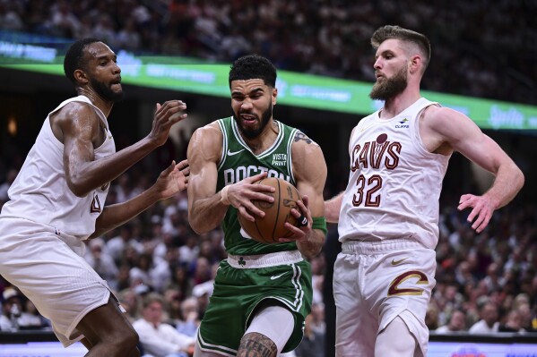 Boston Celtics forward Jayson Tatum, center, drives against Cleveland Cavaliers forwards Dean Wade (32) and Evan Mobley, left, during the second half of Game 4 of an NBA basketball second-round playoff series, Monday, May 13, 2024, in Cleveland. (AP Photo/David Dermer)