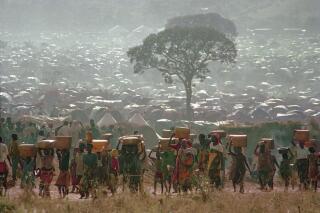 FILE - In this Tuesday, May 17, 1994 file photo, refugees who fled the ethnic bloodbath in neighboring Rwanda carry water containers back to their huts at the Benaco refugee camp in Tanzania, near the border with Rwanda. A report commissioned by the Rwandan government due to be made public on Monday, April 19, 2021 concludes that the French government bears "significant" responsibility for "enabling a foreseeable genocide" that left more than 800,000 dead in 1994 and that that France "did nothing to stop" the massacres. (AP Photo/Karsten Thielker, File)