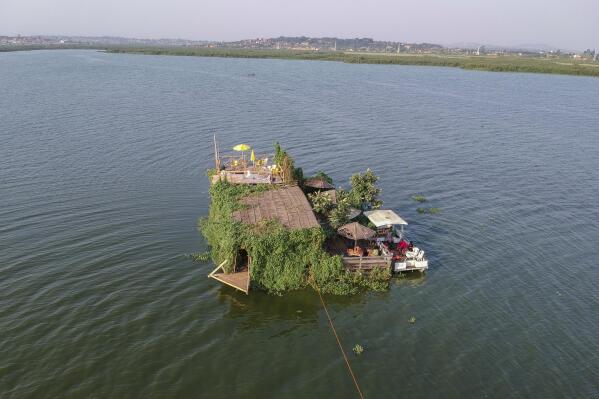 A floating restaurant and bar is seen from the air in Lake Victoria near the Luzira area of Kampala, Uganda Saturday, Feb. 18, 2023. Flowering plants rise from the water into the wooden hull of James Kateeba's boat, used as a floating restaurant and bar that can be unmoored to drift for pleasure, but the greenery emerges from an innovative recycling project which uses thousands of dirt-encrusted plastic bottles to anchor the boat. (AP Photo/Patrick Onen)