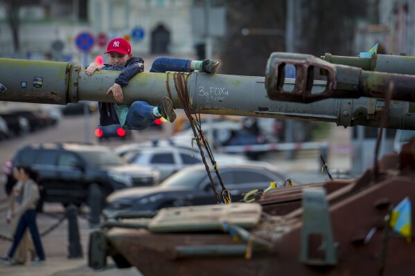 A boy holds on to the barrel of a tank, part of a display of destroyed Russian military equipment, in Kyiv, Ukraine, Sunday, March 31, 2024. (AP Photo/Vadim Ghirda)