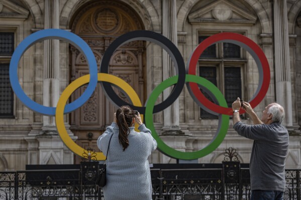 FILE - People take a photograph of the Olympic rings in front of the Paris City Hall, in Paris, on April 30, 2023. Olympic organizers will release 400,000 extra tickets for next year's Paris Games and the Paralympics at the end of the month. Organizers said Wednesday Nov. 22, 2023 the sale will start on Nov. 30 at 10 a.m. on the official ticketing website, with seats available for all sports except surfing, in all price categories. Tickets will be sold on a first come-first serve basis, without a lottery. (AP Photo/Aurelien Morissard, File)