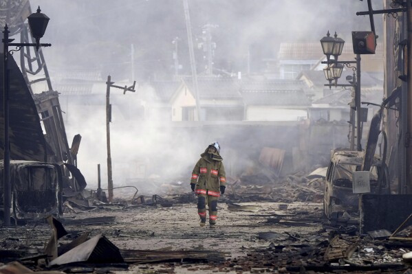 A firefighter walks through the rubble and wreckage of a burnt-out marketplace following earthquake in Wajima, Ishikawa prefecture, Japan Tuesday, Jan. 2, 2024. (Kyodo News via AP)