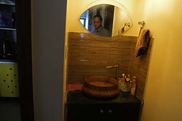 S. Prasad, who lives with his wife and two children in a housing society, is reflected in the mirror as he shows the tap with no running water inside his apartment, in Bengaluru, India, Monday, March 11, 2024. (AP Photo/Aijaz Rahi)
