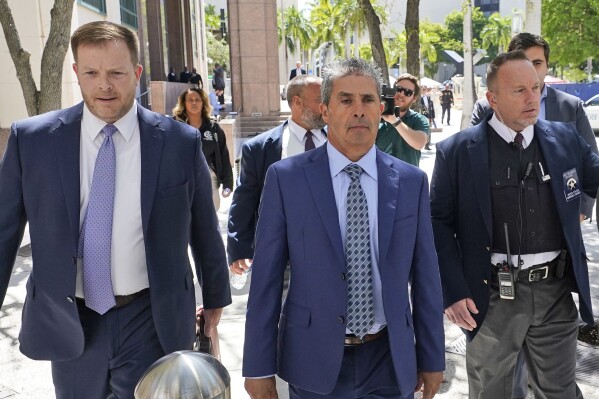 Carlos De Oliveira, center, an employee of Donald Trump's Mar-a-Lago estate, leaves a court appearance with attorney John Irving, left, at the James Lawrence King Federal Justice Building, Monday, July 31, 2023, in Miami. De Oliveira, Mar-a-Lago's property manager, was added last week to the indictment with Trump and the former president's valet, Walt Nauta, in the federal case alleging a plot to illegally keep top-secret records at Trump's Florida estate and thwart government efforts to retrieve them. (AP Photo/Wilfredo Lee)