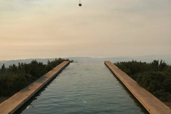 
              In this photo provided by the Santa Barbara County Fire Department, a helicopter making a water drop run flies over an infinity pool behind a home off Bella Vista Dr. in Montecito, Calif., Wednesday, Dec. 13, 2017. After announcing increased containment on the Thomas fire, one of the biggest wildfires in California history, officials Wednesday warned that communities remain at risk and the threat could increase as unpredictable winds whip up again. (Mike Eliason/Santa Barbara County Fire Department via AP)
            