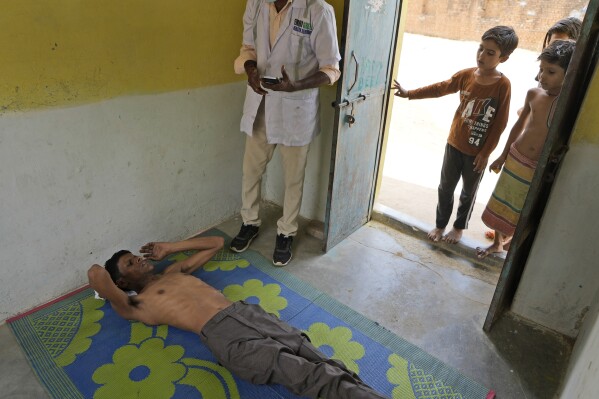 Jitendra Kumar, a paramedic, center, talks to a patient, left, who is suffering from a heat stroke before carrying him to his ambulance from his home in village Mirchwara, 24 kilometers (14.91 miles) from Banpur in Indian state of Uttar Pradesh, Saturday, June 17, 2023. Ambulance drivers and other healthcare workers in rural India are the first line of care for those affected by extreme heat. (AP Photo/Rajesh Kumar Singh)