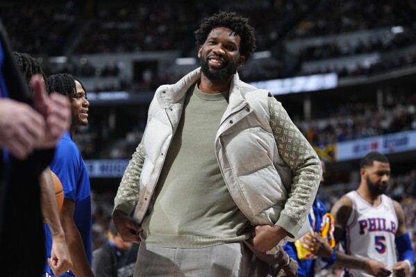 Scratched before the start of the game, Philadelphia 76ers center Joel Embiid jokes with teammates during a time out in the second half of an NBA basketball game against the Denver Nuggets, Saturday, Jan. 27, 2024, in Denver. (AP Photo/David Zalubowski)