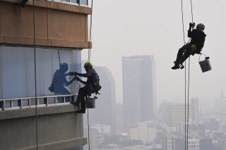 Limpiadores de ventanas están suspendidos de cuerdas en un edificio de apartamentos de gran altura en la Ciudad de México, el miércoles 13 de diciembre de 2023. (AP Foto/Marco Ugarte)