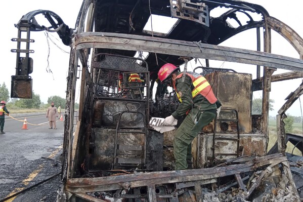 In this photo released by the Rescue 1122 Emergency Department, rescue workers examine a burnt bus at the accident site on a highway in Pindi Bhattian, Pakistan, Sunday, Aug. 20, 2023. A bus in Pakistan caught fire after hitting a van parked on the shoulder of an intercity highway in eastern Punjab province, killing multiple people and injuring others, police and rescue officials said Sunday. (Rescue 1122 Emergency Department vis AP)