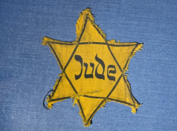 FILE - In this Wednesday, Jan. 22, 2014 file photo, the Yellow Star badge of Heinz-Joachim Aris (Dresden 1941) reading 'Jew' is displayed in a showcase during a press preview in the new special exhibition 'Shoes of the Dead - Dresden and the Shoah' at the Military History Museum in Dresden, Germany. Before local anti-Jewish laws were enacted, before neighborhood shops and synagogues were destroyed, and before Jews were forced into ghettos, cattle cars, and camps, words were used to stoke the fire of hate. 'ItStartedWithWords' is a digital, Holocaust education campaign posting weekly videos of survivors from across the world reflecting on those moments that led up to the Holocaust. (AP Photo/Jens Meyer, file)