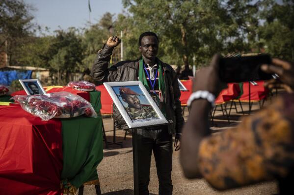 A man poses for a picture as he stands next to the coffin containing the remains of Burkina Faso's revolutionary leader, Thomas Sankara, during his reburial ceremony in Ouagadougou, Burkina Faso, Thursday, Feb. 23, 2023. Sankara, was reburied, eight years after his body was exhumed as part of an investigation. The revolutionary leader and twelve others were gunned down in the capital, Ouagadougou, during a 1987 coup and buried hastily, their bodies only allowed to be dug up in 2015, after the ousting of former President Blaise Compaore, who ruled the country with an iron fist for nearly 30 years and prevented the exhumation. (AP Photo/Sophie Garcia)