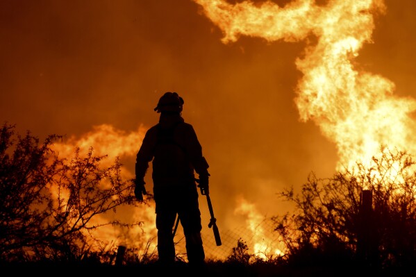 A firefighter is silhouetted by the flames of a forest fire on the outskirts of Villa Carlos Paz, Argentina, Tuesday, Oct. 10, 2023. (AP Photo/Nicolas Aguilera)
