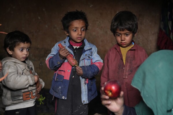 Three internally displaced children look with surprise at an apple that their mother brought home after begging, in a camp on the outskirts of Kabul, Afghanistan, Thursday, Feb 2, 2023. Since the chaotic Taliban takeover of Kabul on Aug. 15, 2021, an already war-devastated economy once kept alive by international donations alone is now on the verge of collapse. (AP Photo/Ebrahim Noroozi)