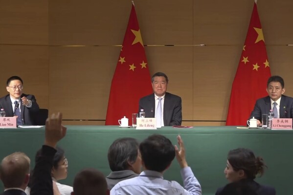 Vice minister of Finance Liao Min, left, gestures toward a journalist at a news conference at the Chinese mission to the World Trade Organization in Geneva, Switzerland, Sunday, May 11, 2025, alongside Vice Premier He Lifeng and Li Chenggang, vice minister of commerce. (AP Photo/Jamey Keaten)