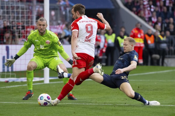 Munich's Harry Kane, center, vies for the ball with Mainz's Andreas Hanche Olsen, right and goalkeeper Robin Zentner, during the German Bundesliga soccer match between Bayern Munich and Mainz, at the Allianz Arena stadium, in Munich, Germany, Saturday, March 9, 2024. (Sven Hoppe/dpa via AP)