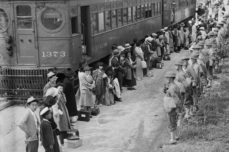 In this photo provided by the National Archives, Japanese Americans from San Pedro, Calif., arrive at the Santa Anita Assembly Center in Arcadia, Calif., on April 5, 1942. People were temporarily housed at this center at the Santa Anita race track before being moved inland to internment camps during World War II. (Clem Albers/War Relocation Authority/National Archives via AP)