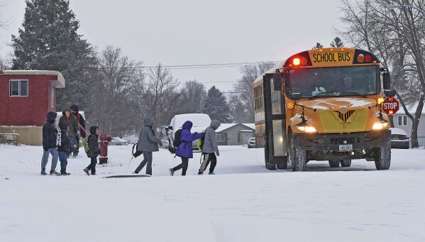 Children in winter coats line up to get into a school bus Thursday, March 21, 2024 in Bismarck, N.D. Parts of Montana, the Dakotas, Minnesota, Illinois and Wisconsin are under winter weather advisories, with snow expected to start falling Thursday in some areas. Minnesota could see a foot of snow over the weekend, and parts of New England could also see 12 to 18 inches (30 to 45 centimeters) in the coming days. (Tom Stromme/The Bismarck Tribune via AP)