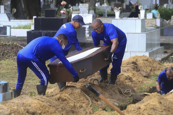 Cemetery workers lower into a grave, a coffin that contains the remains of an unidentified migrant, at the Sao Jorge cemetery, in Belem, Para state, Brazil, Thursday, April 25, 2024. The bodies of nine migrants found on an African boat off the northern coast of Brazil's Amazon region were buried Thursday with a solemn ceremony. (AP Photo/Paulo Santos)