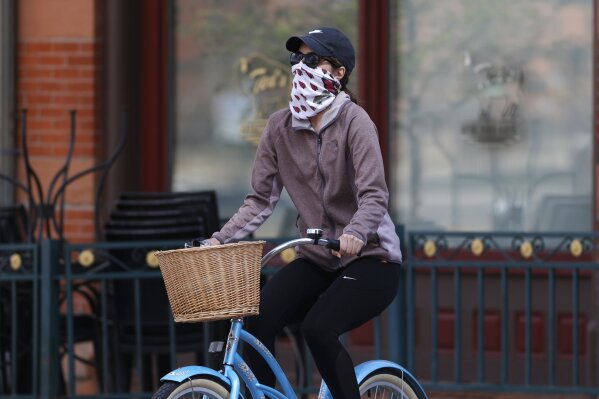 A bicyclist wears face protection against the new coronavirus while pedaling through Larimer Square early Saturday, April 25, 2020, in downtown Denver. (AP Photo/David Zalubowski)
