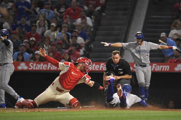 Toronto Blue Jays' George Springer, second from right, scores under the tag of Los Angeles Angels catcher Logan O'Hoppe, second from left, on a throwing error by O'Hoppe as Anthony Santander, left, and Ernie Clement, right, gesture while home plate umpire Tom Hanahan watches during the sixth inning of a baseball game Thursday, May 8, 2025, in Anaheim, Calif. (AP Photo/Mark J. Terrill)