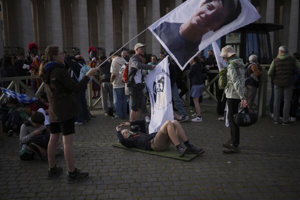 A faithful waves a flag with Carlo Acutis, the 15-year-old Italian boy who died in 2006 of leukemia and beatified in 2020, at the funeral of Pope Francis in St. Peter's Square at the Vatican, Saturday, April 26, 2025. (AP Photo/Emilio Morenatti)