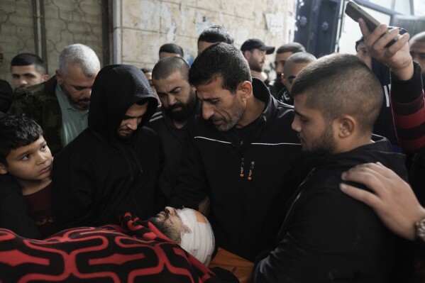 Palestinian stand around the body of a man killed during Israeli military raid on Nur Shams refugee camp in the West Bank on Sunday, Dec. 17, 2023. (AP Photo/Majdi Mohammed)