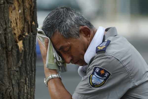 A security guard wearing an electric fan on his neck wipes his sweat on a hot day in Beijing, Monday, July 3, 2023. (AP Photo/Andy Wong, File)