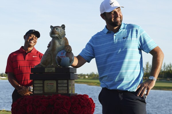 Scottie Scheffler, of the United States, right, poses with the trophy as Tiger Woods smiles in the background, after winning the Hero World Challenge PGA Tour at the Albany Golf Club in New Providence, Bahamas, Sunday, Dec. 3, 2023. (AP Photo/Fernando Llano)