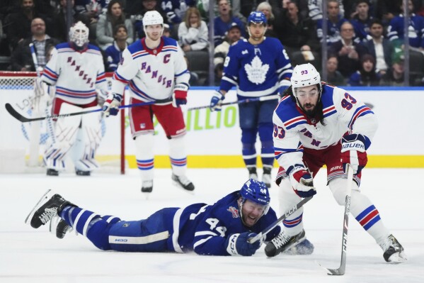 New York Rangers forward Mika Zibanejad (93) protects the puck from a diving Toronto Maple Leafs defenseman Morgan Rielly (44) during the third period of an NHL hockey game Tuesday, Dec. 19, 2023, in Toronto. (Nathan Denette/The Canadian Press via AP)