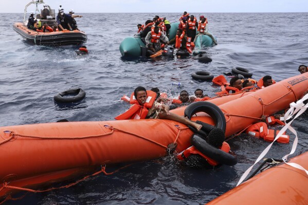 FILE - Migrants aboard a rubber boat end up in the water while others cling on to a centifloat before being rescued by a team of the Sea Watch-3, around 35 miles away from Libya, Monday, Oct. 18, 2021. A majority of European Union countries are calling for more agreements with countries that people leave or transit to get to Europe, saying that to tackle irregular migration and manage migration movements to the 27-member bloc. (AP Photo/Valeria Mongelli, File)