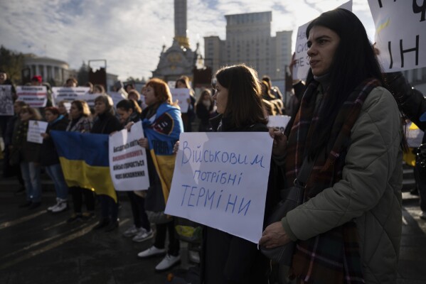 Relatives of soldiers hold a poster reading "Soldiers need terms of service" while attending a meeting on Independence square in Kyiv, Ukraine, Friday, Oct. 27, 2023. Families of Ukrainian servicemen gathered to demand their loved ones return home after serving 18 months in the military as the war with Russia nears its second year. (AP Photo/Alex Babenko)