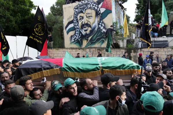 Mourners carry the coffin of Saleh Arouri, one of the top Hamas commanders, who was killed in an apparent Israeli strike Tuesday, as they pass in front of a graffiti that shows late Palestinian leader Yasser Arafat, during his funeral in Beirut, Lebanon, Thursday, Jan. 4, 2024. (AP Photo/Hussein Malla)