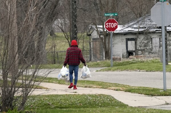 A Flint, Mich., resident walks home after picking up food from a food bank, Tuesday, March 19, 2024, in Flint. (AP Photo/Carlos Osorio)