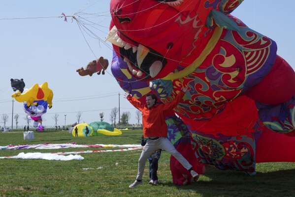 A visitor poses in front of a giant kite at the 41st International Kite Festival in Weifang, Shandong Province of China, Saturday, April 20, 2024. (AP Photo/Tatan Syuflana)