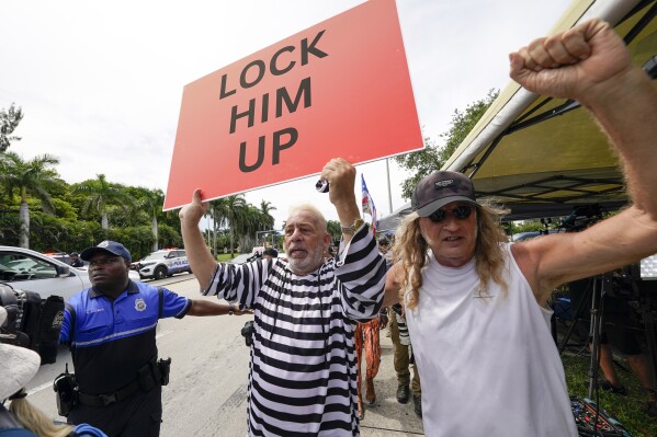 Demonstrators hold signs outside Trump National Doral resort in Doral, Fla., Monday, June 12, 2023, before former President Donald Trump arrives. (AP Photo/Gerald Herbert)