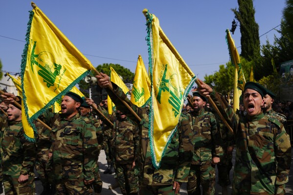 Los combatientes de Hezbolá izan la bandera de su grupo y gritan consignas mientras asisten a la procesión fúnebre del combatiente de Hezbolá, Bilal Nemr Rmeiti, quien fue asesinado por bombardeos israelíes, durante su procesión fúnebre en la aldea de Majadel, en el sur del Líbano, el domingo 22 de octubre de 2023. (Foto AP/Hassan Ammar)